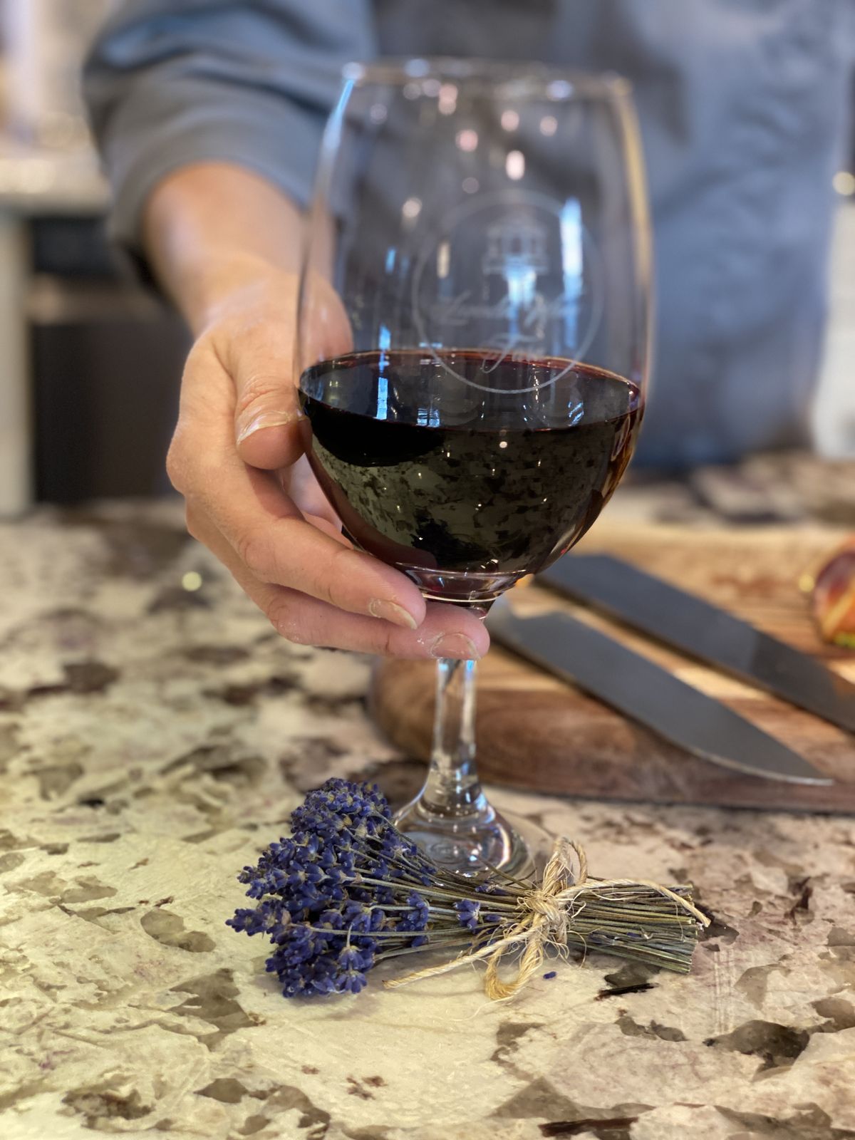 A hand raising a glass of red wine over a lavender bundle